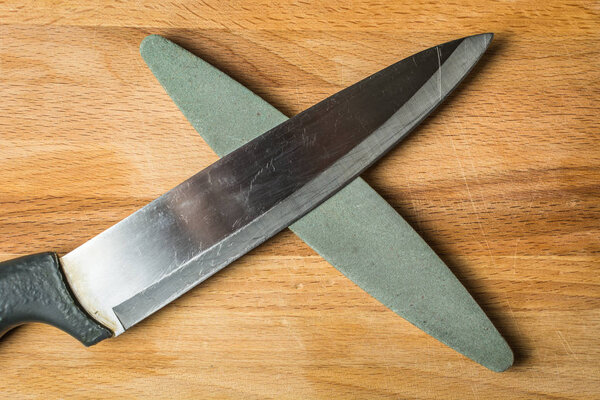 Large kitchen knife for vegetables with grindstone made of coarse abrasive on wooden board.