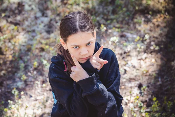 Ernstes Mädchen im warmen Pullover zeigt im Kiefernwald die Finger in Gesichtsnähe. — Stockfoto