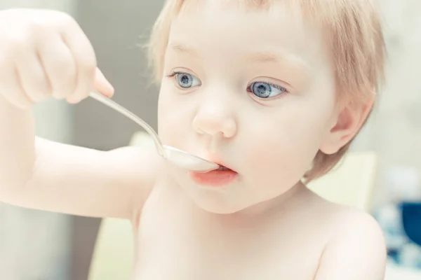 Симпатична дитина з блакитними очима п'є чай з ложки на кухні . — стокове фото