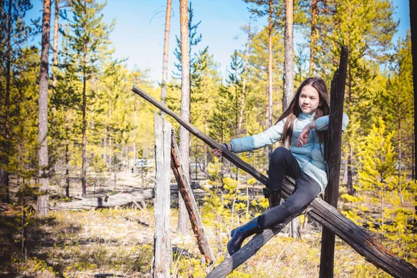 The beautiful girl in light jacket sits and has rest on an old snag in the spring forest. — Stock Photo, Image