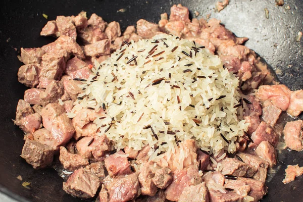 Long grain rice and pieces of beef are laid in cast iron cauldron for cooking pilaf. — Stock Photo, Image