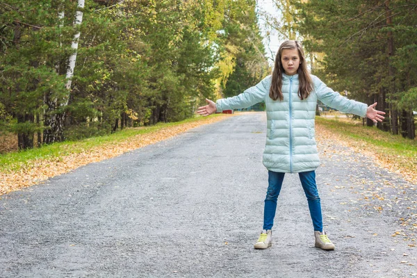 秋に道路に広がる手を持つダウンジャケットの女の子. — ストック写真