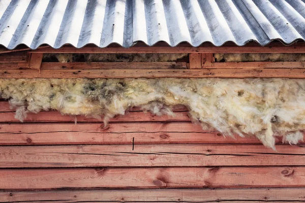 Warm glass wool sticks out from the roof of wooden house during unfinished construction. — Stock Photo, Image