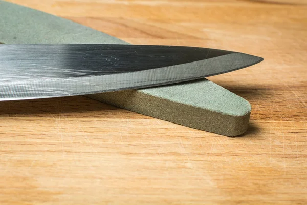 Cuchillo de cocina de acero para verduras con muela de abrasivo grueso sobre tabla de madera . —  Fotos de Stock