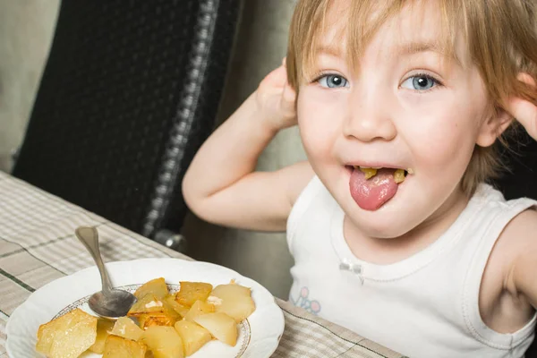 Маленький ребенок с красивыми глазами ест картошку за кухонным столом . — стоковое фото