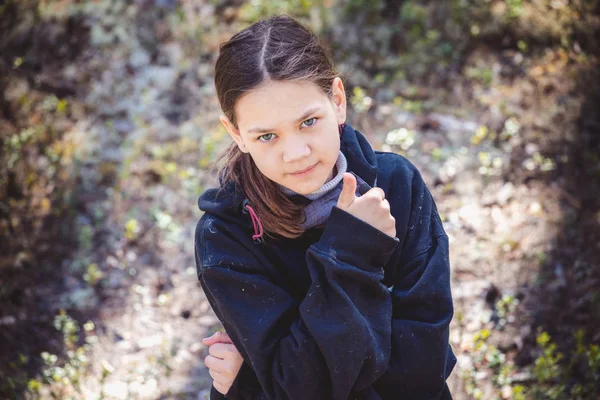 Schattig meisje in warme trui toont haar vinger top in de buurt van het gezicht in Pine Forest. — Stockfoto