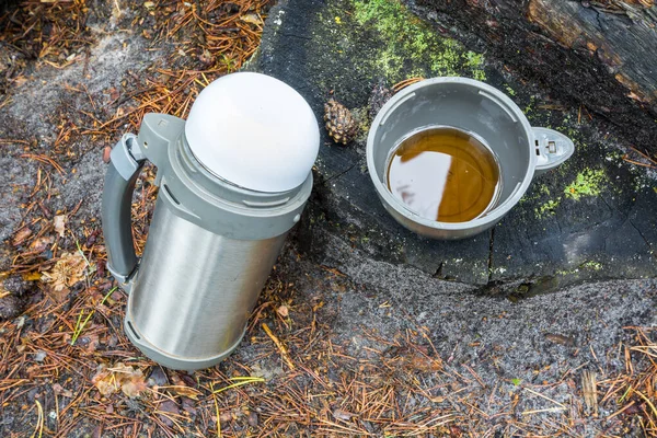 Grand thermos de randonnée avec tasse de thé se tient sur souche dans la forêt . — Photo