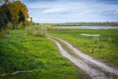 Yeşil çimlerden nehir kıyısına giden kumlu yol.