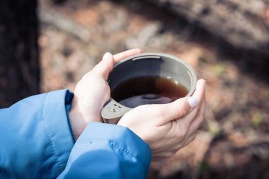 Ormanda yürüyüş yaparken ısınmak için kızın elinde çay olan termostan bir kupa çay..