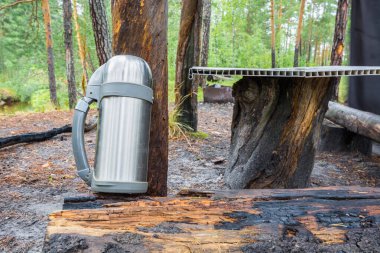 Sıcak çay ya da kahve için demir yürüyüş termosu ormandaki ağaç ve masanın yanında..
