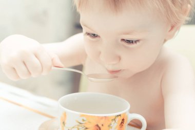 Mavi gözlü sevimli çocuk mutfakta bir kaşıkçay içme.
