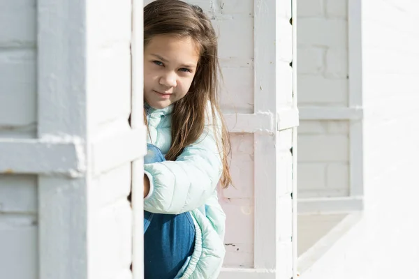 Чарівна дівчина з тече волоссям у блакитній куртці сидить і обіймає коліна руками на тлі білої цегляної стіни . — стокове фото