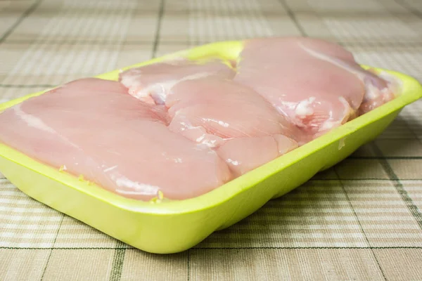 Raw chicken breast fillet lies in plastic green packaging on the kitchen table. — Stock Photo, Image