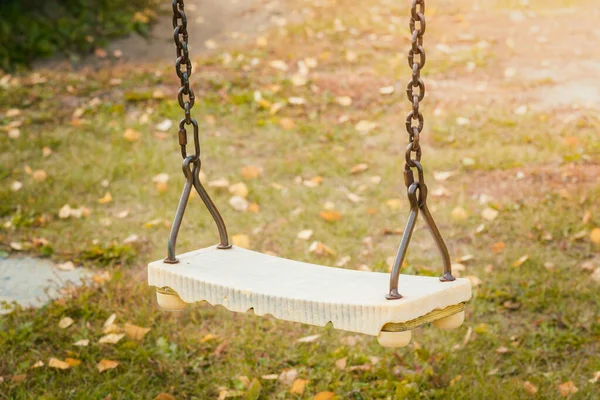 Childrens swing on iron chains for riding and entertainment with yellow foliage on ground in autumn day.