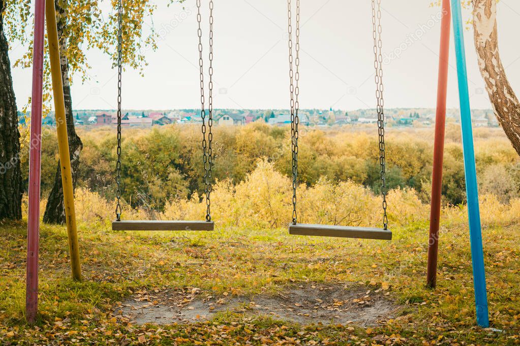 Childrens swing on iron chains for riding and entertainment with yellow foliage on ground in autumn day.