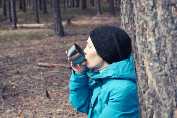 在森林里徒步旅行时 手里拿着一杯加茶的热水瓶来取暖 — 图库照片