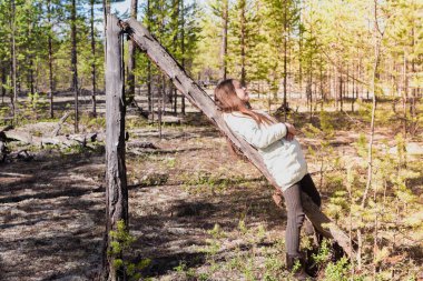 Uzun bir yürüyüşten sonra ceketli yorgun kız çam ormanındaki eski pürüzlerin üzerinde dinleniyor.
