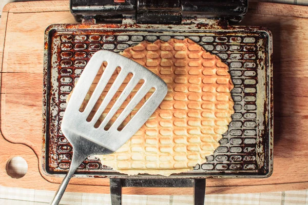 Frying waffles in waffle iron with iron spoon for turning on kitchen table