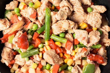 Tavada sebze karışımlı kızarmış tavuk parçaları.