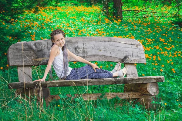 彼女の頭の上に恐ろしいですコンテンツの女の子は 森林の花の背景を背景にベンチに休んでいます — ストック写真