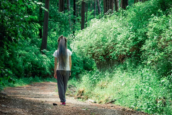 美しいです女の子とともに長いですドレッドロックオン彼女の頭は森の道に沿って歩いている — ストック写真