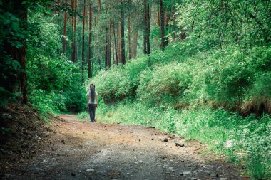Kafasında uzun kazayağı olan güzel bir kız orman yolunda yürüyor.