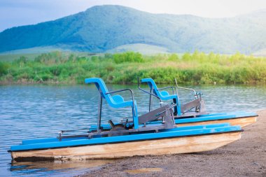 Yüksek dağların arka planında su üzerinde sürmek için pedallarla yürüyen katamaran.