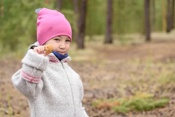 帽子の小さな子供は寒い秋の日に松林の中で食用キノコを手に持っています — ストック写真