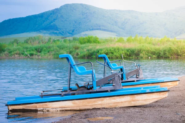 Yüksek dağların arka planında su üzerinde sürmek için pedallarla yürüyen katamaran.