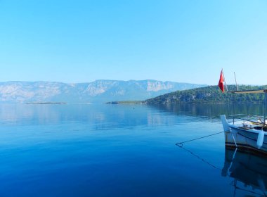 Deniz suyunda yelkenli. Rıhtımda yelkenli. Tekne kıyıya yakın yüzüyor. Türk bayrağı