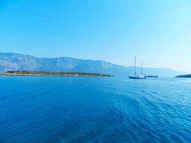 Deniz suyunda yelkenli. Tekne kıyıya yakın yüzüyor. Kıyıdan uzakta demirli yatlar. deniz manzarası ve dağlar