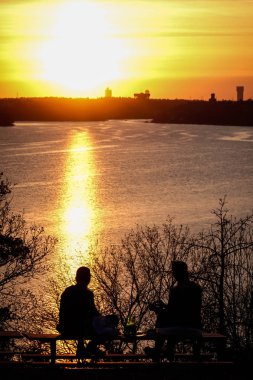 Stockholm, İsveç Lidingo adasında gün batımında iki adam bir tepede bira içiyor..