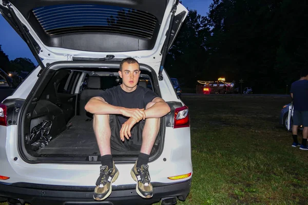 Amenia New York USA An 18 year old teenager sits on a tailgate at a  drive-in movie theatre.