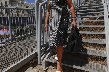 Syracuse, Sicily, Italy A woman in a metallic-looking dress descends metal steps to the beach on Ortygia island. clipart