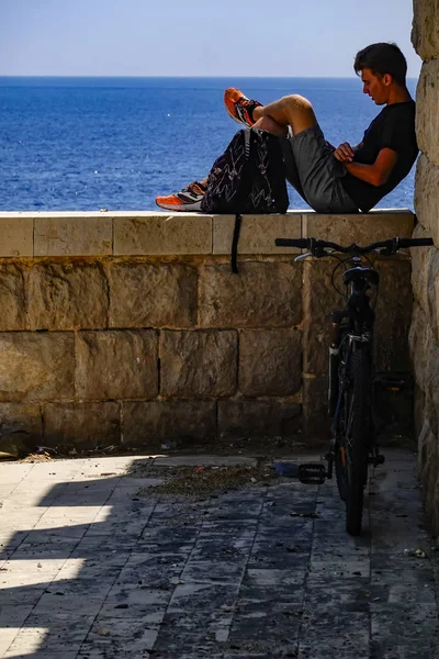 シラキュース シチリア イタリア 地中海を見下ろす壁に一人で座っている若者 — ストック写真