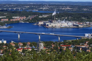 Sundsvall, İsveç, yerel bir dağ tepesinden şehir manzarası ve ön planda bir kağıt fabrikası.
