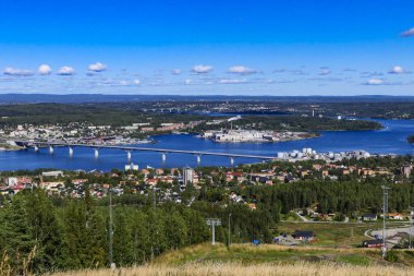 Sundsvall, İsveç, yerel bir dağ tepesinden şehir manzarası ve ön planda bir kağıt fabrikası.