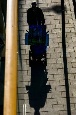 Stockholm, İsveç. Bebek arabasıyla yürüyen bir adam kaldırımda güçlü gölgeler içinde bir şeyler taşıyor..