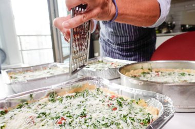 Bir kadın evde ıspanaklı domatesli kiş yapar ve parmesan peyniri rendeler..