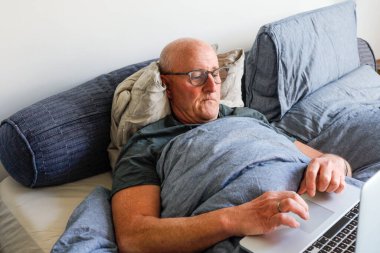 Dizüstü bilgisayarla yatakta yatan bir adam..