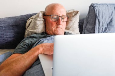 Dizüstü bilgisayarla yatakta yatan bir adam..