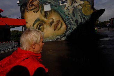 Sunne, Sweden Pedestrians on a squre in front of a large face wall painting.