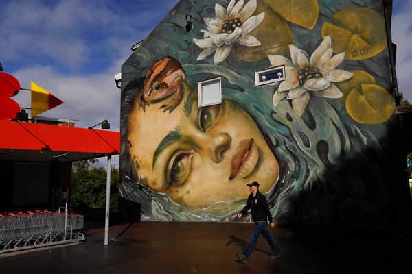 Sunne, Sweden Pedestrians on a squre in front of a large face wall painting.