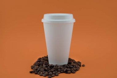 Kahve çekirdekleri, turuncu arka plan üzerinde kağıt kahve bardağı. Kahve bardağı kaplıdır.