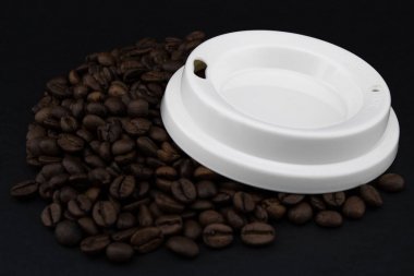 Kahve çekirdekleri üzerinde kağıt kahve bardağı kapağı, siyah arka plan.