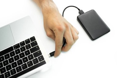 Onun laptop, beyaz masa harici bir sabit disk bağlayan bir kişinin el.