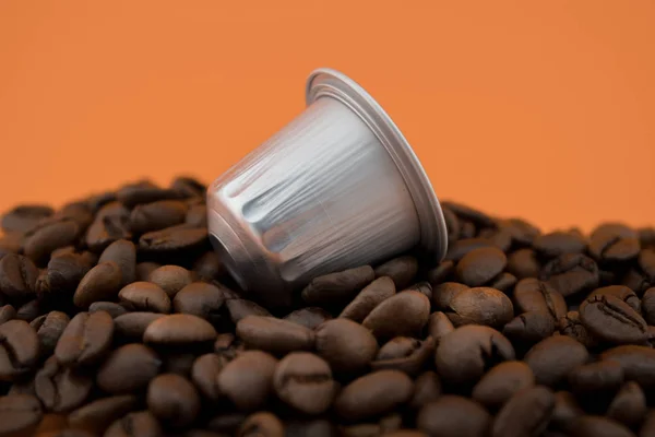 Espresso coffee capsule or coffee pod on coffee beans, orange background.