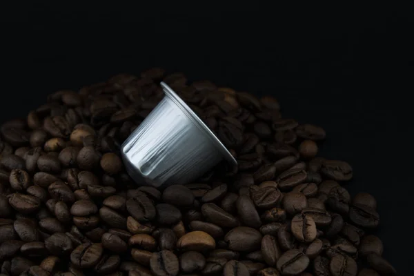 Capsule di caffè o cialde di caffè su chicchi di caffè, sfondo nero. Capsule . — Foto Stock