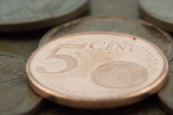 Macro of a five euro cent coin supported on more bronze coins.