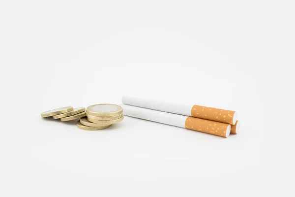 Varios cigarros y una pila de monedas sobre fondo blanco. Gastos económicos . —  Fotos de Stock